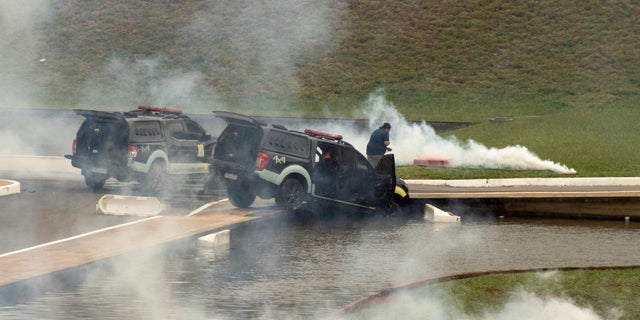 Police cars are pictured amidst tear gas after being pushed off the road by supporter of Brazil's far-right former President Jair Bolsonaro who dispute the election of leftist President Luiz Inacio Lula da Silva, during protests, in Brasilia, Brazil January 8, 2023. REUTERS/Antonio Cascio NO RESALES. NO ARCHIVES