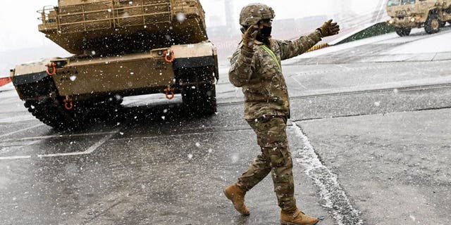 A U.S. Army soldier signals the way to a M1A2 Abrams battle tank that will be used for military exercises by the 2nd Armored Brigade Combat Team at the Baltic Container Terminal in Gdynia, Poland, on Dec. 3, 2022.