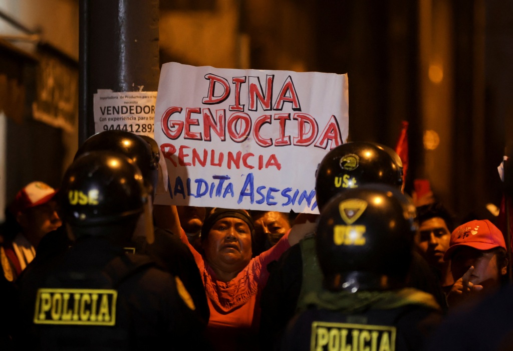 A protester holds a sign that translates to "Genocidal Dina, resign, bloody murderer," on Jan. 20, 2023.
