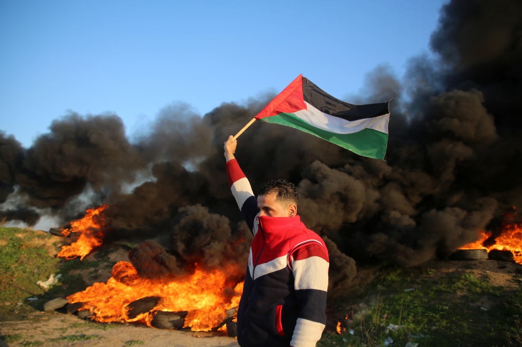 A Palestinian man holds a Palestinian flag during clashes with Israeli forces, near the Israel-Gaza border east of Gaza City, on Jan. 26, 2023.