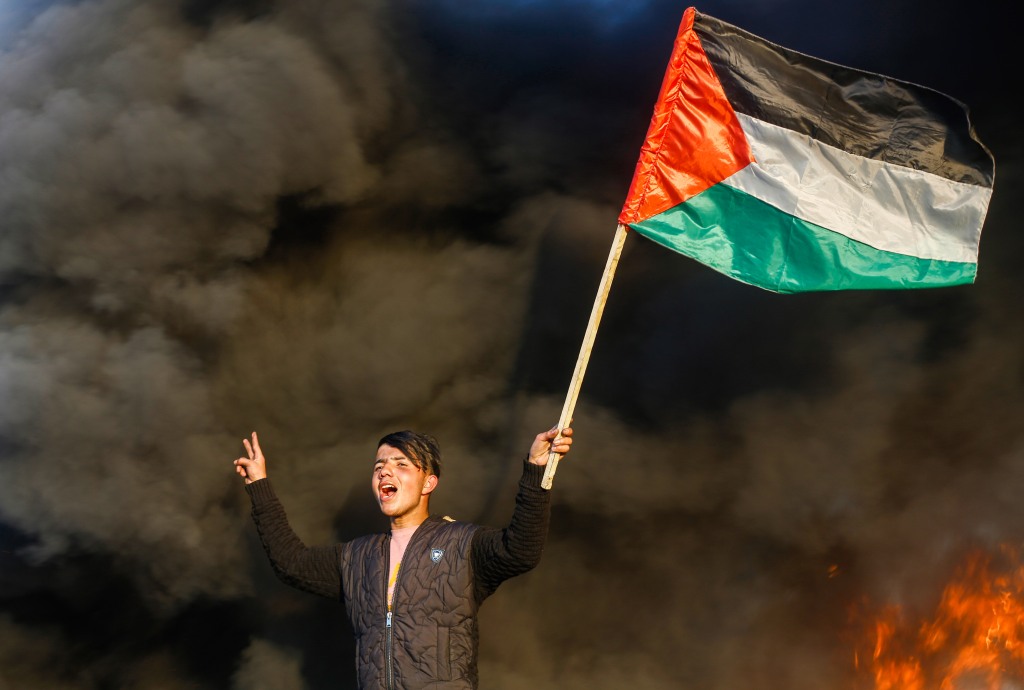 A Palestinian man holds a Palestinian flag during the clashes with Israeli forces, near the Israel-Gaza border east of Gaza City.