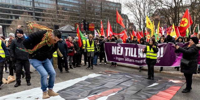 A protestor prepares to jump on a banner with the image of Turkish President Recep Tayyip Erdogan during a demonstration organized by The Kurdish Democratic Society Center in Sweden, as Sweden seeks Turkey's approval to join NATO, in Stockholm, Saturday, Jan. 21, 2023. (Christine Olsson/TT News Agency via AP)