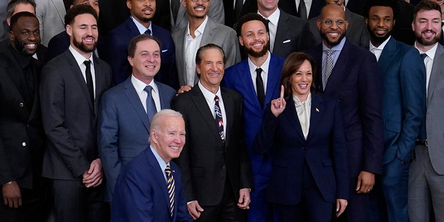 President Joe Biden kneels during a group photo with Vice President Kamala Harris and members of the 2022 NBA champions, the Golden State Warriors, during an event in the East Room of the White House in Washington, Tuesday, Jan 17, 2023.