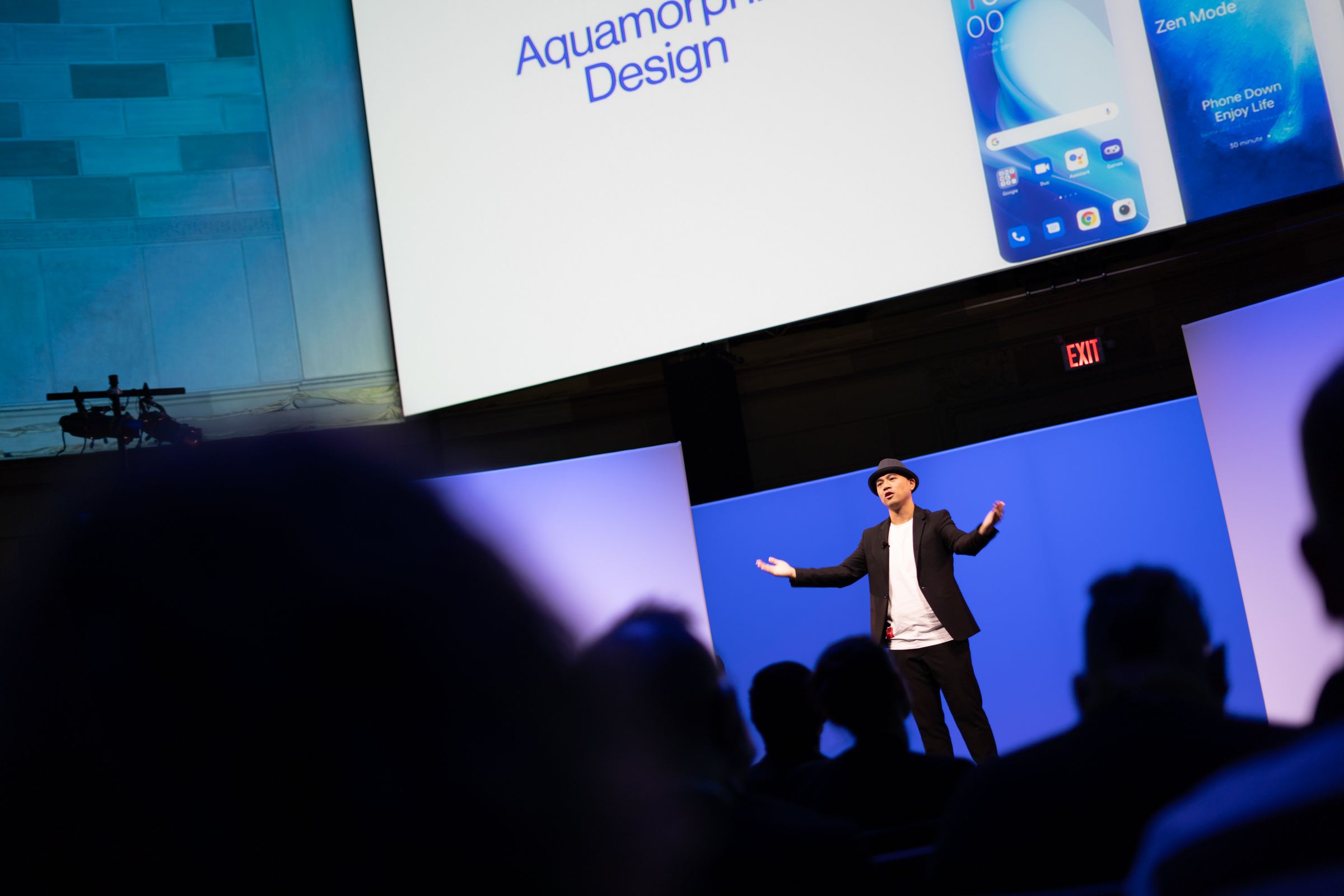 OnePlus executive presenting on stage with audience in silhouette in the foreground.