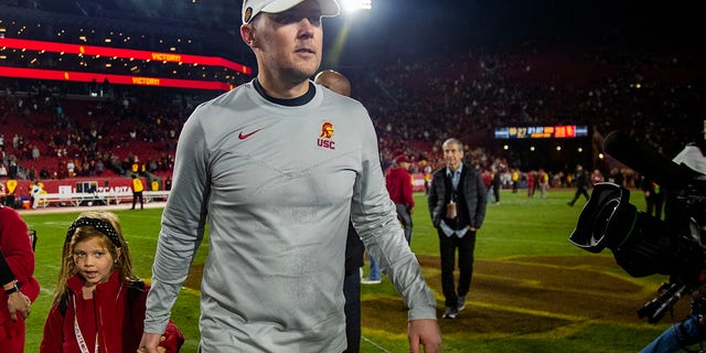 USC head coach Lincoln Riley holds his daughter's hand as he leaves the field after the Trojans beat Notre Dame at the Coliseum on Nov. 26, 2022, in Los Angeles.