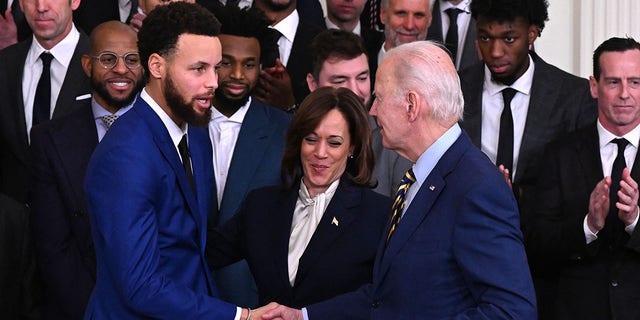 U.S. President Joe Biden (R) shakes hands with Golden State Warriors basketball player Stephen Curry (L) as U.S. Vice President Kamala Harris (C) looks on during a celebration for the Golden State Warriors 2022 NBA championship, in the East Room of the White House in Washington, DC, on January 17, 2023. 