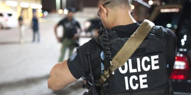 An Immigrations and Customs Enforcement officer preparing for an arrest in a parking lot.