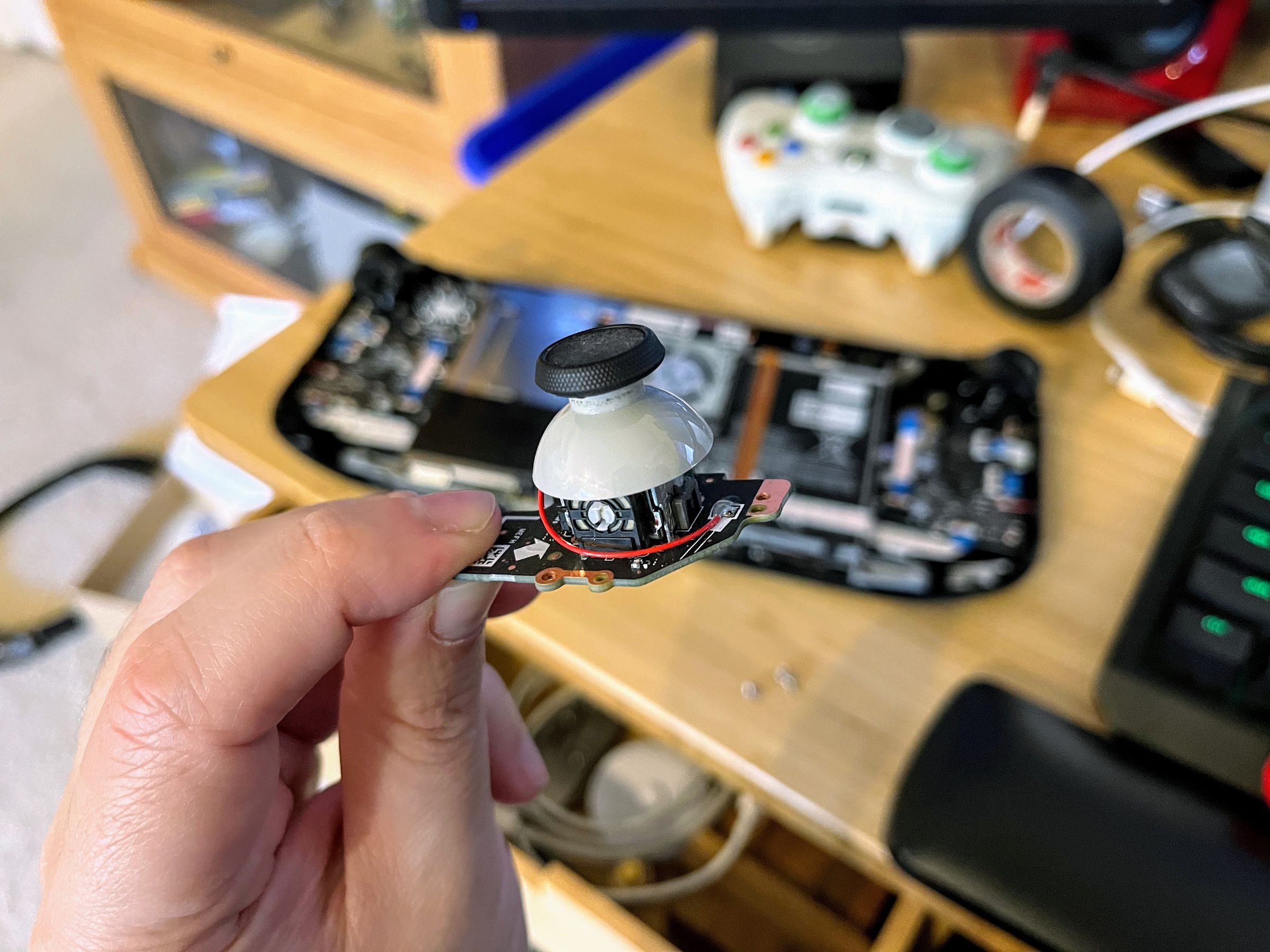 A person holds a Steam Deck joystick above a deconstructed Steam Deck on a desk.