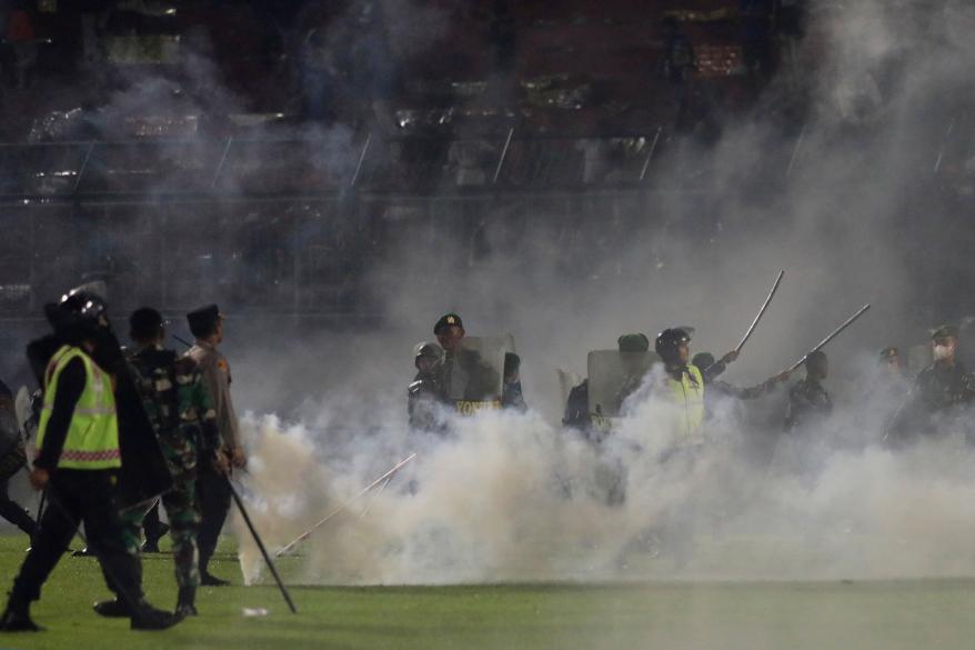 Police officers and soldiers stand amid tear gas smoke during a soccer match at Kanjuruhan Stadium in Malang, East Java, Indonesia, on Oct. 1, 2022.