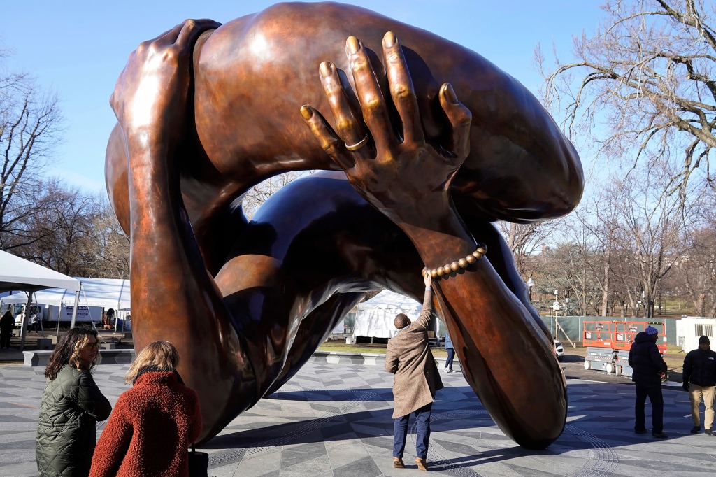 A man reaches to touch a detail of the 20-foot-high bronze sculpture "The Embrace," a memorial to Dr. Martin Luther King Jr. and Coretta Scott King, in the Boston Common, Tuesday, Jan. 10, 2023, in Boston.