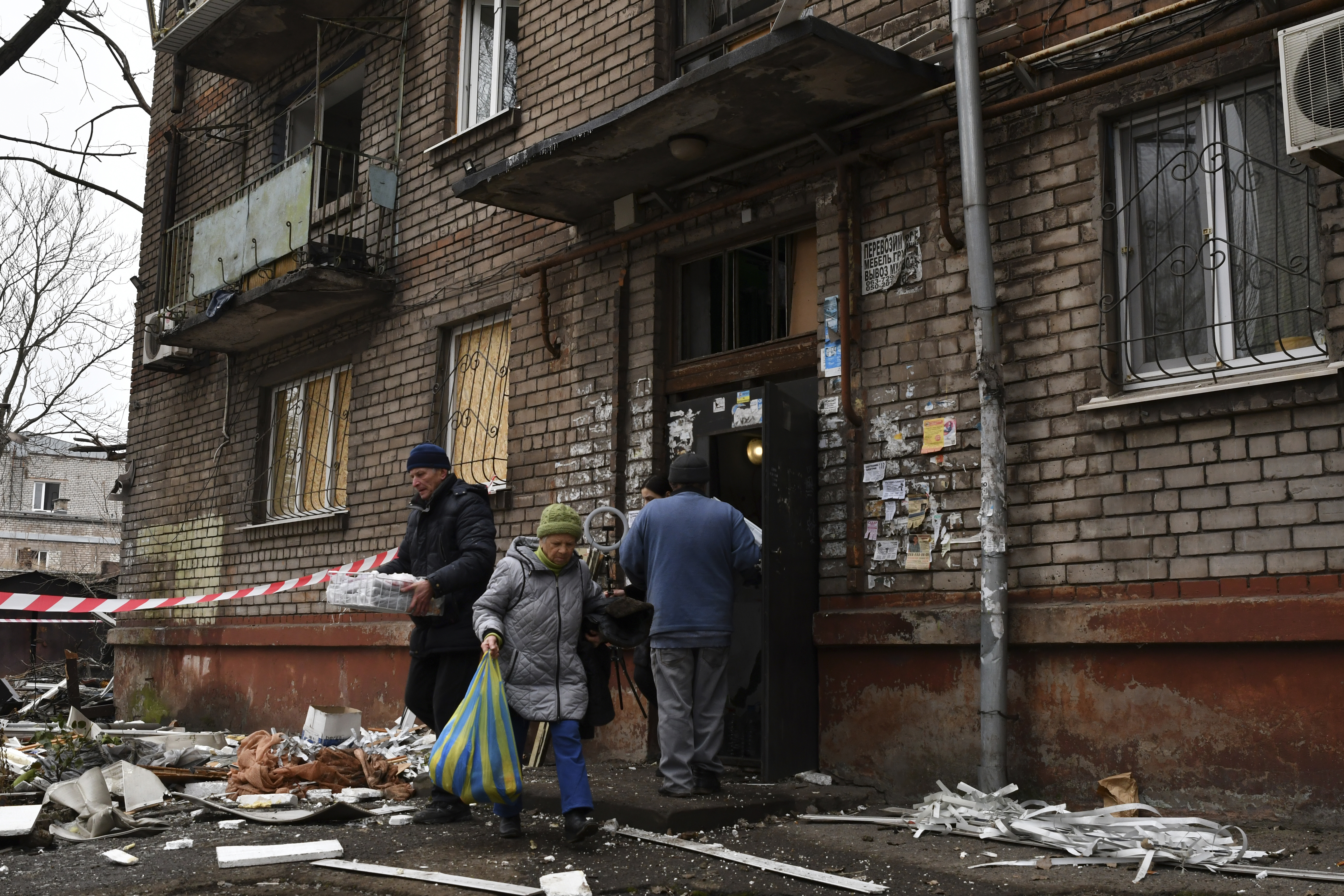 Local residents carry their belongings as they leave their home damaged in the night Russian rocket attack.