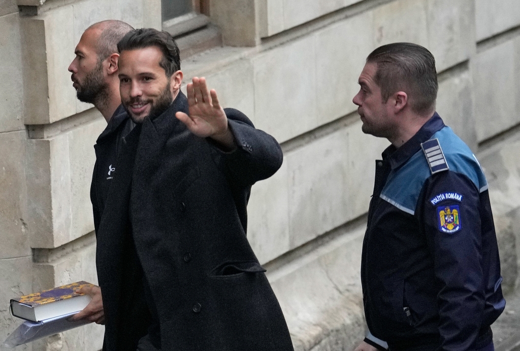 Tristan Tate waves to the media as he and his brother, Andrew Tate, are brought by police officers to the Court of Appeal, in Bucharest, Romania, on Jan.10, 2023. 