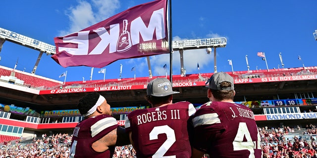 Nathaniel Watson #14, Will Rogers III #2, and Jett Johnson #44 of the Mississippi State Bulldogs wave a Mike flag in memory of Mike Leach after defeating the Illinois Fighting Illini 19-10 in the ReliaQuest Bowl at Raymond James Stadium on January 02, 2023 in Tampa, Florida.