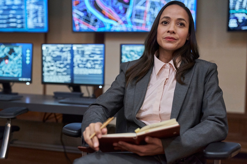 Dania Ramirez in "Alert: Missing Persons Unit" sitting holding a binder. 