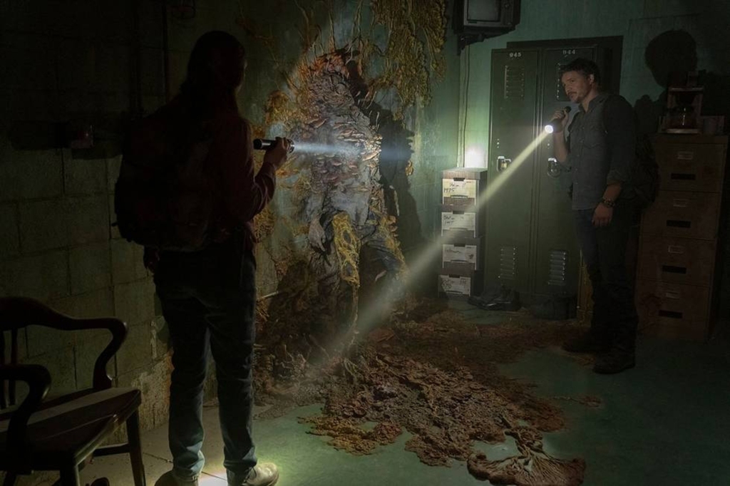 Anna Torv and Pedro Pascal in "The Last of Us" shining flash lights i a dark room. 