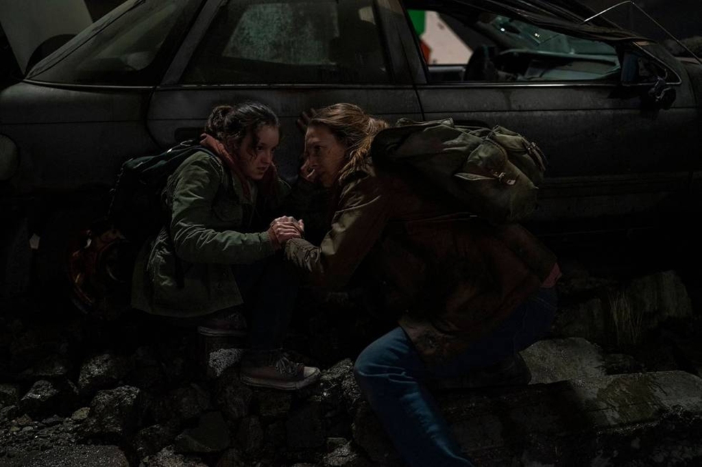 Bella Ramsey and Anna Torv in "The Last of Us" crouching in a dark room. 