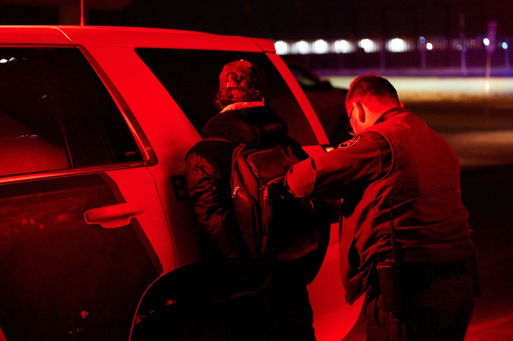 A cop presses a migrant against his vehicle as he handcuffs him