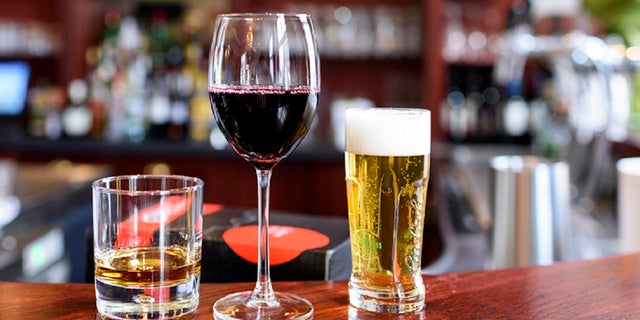 A glass of wine, beer and whiskey on top of a bar.