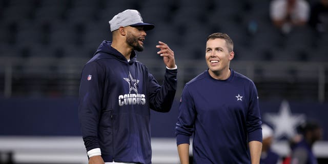 Quarterback Dak Prescott #4 of the Dallas Cowboys talks with offensive coordinator Kellen Moore of the Dallas Cowboys on the field during pregame warm-ups before the Dallas Cowboys take on the Houston Texans in a preseason NFL game at AT&amp;amp;T Stadium on August 21, 2021 in Arlington, Texas.