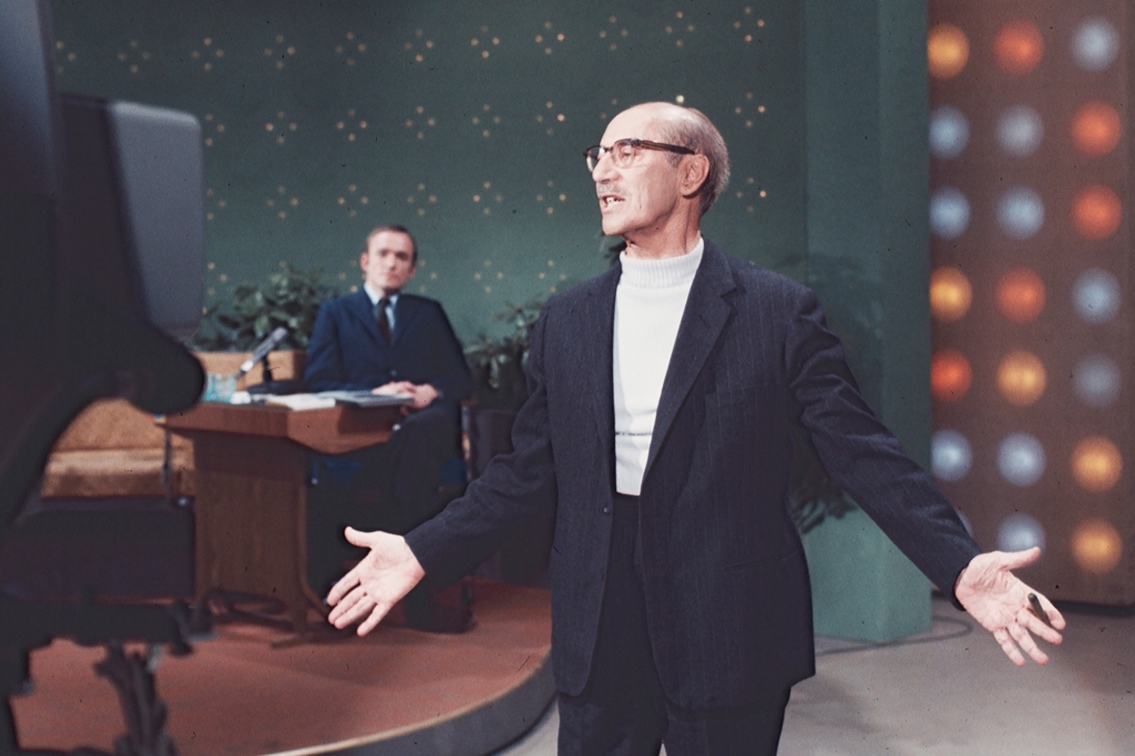 Groucho Marx singing a song on "The Dick Cavett Show" in 1967. He's got a cigar in his hand and has his arms out in front of him. Cavett is in the background seated behind his desk.