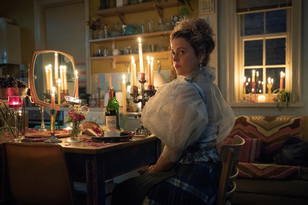 Jen (Mairead Tyers) in "Extraordinary" sitting at a desk wearing a dress. 