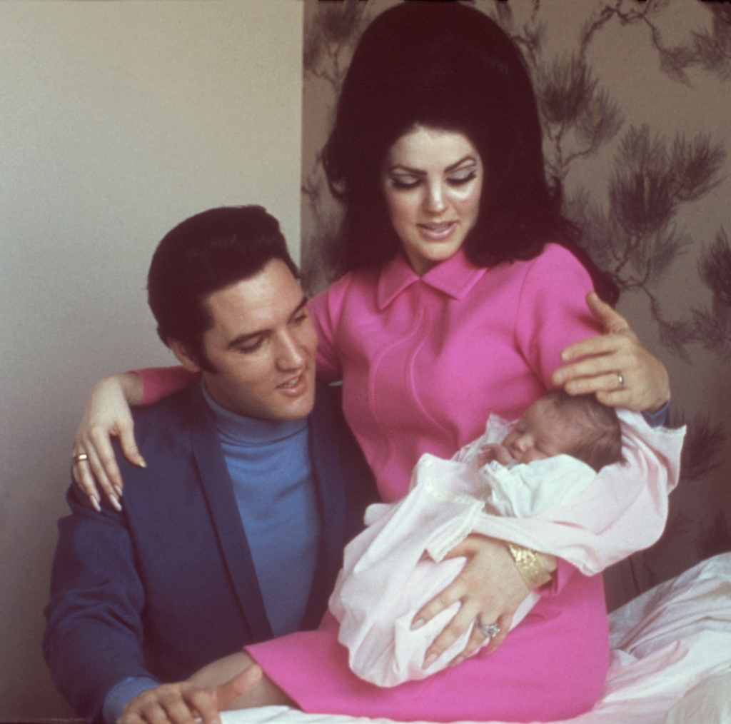  Elvis Presley with his wife Priscilla Presley and their 4 day old daughter Lisa Marie Presley in 1968. They sit on the bed holding a baby, smiling. 