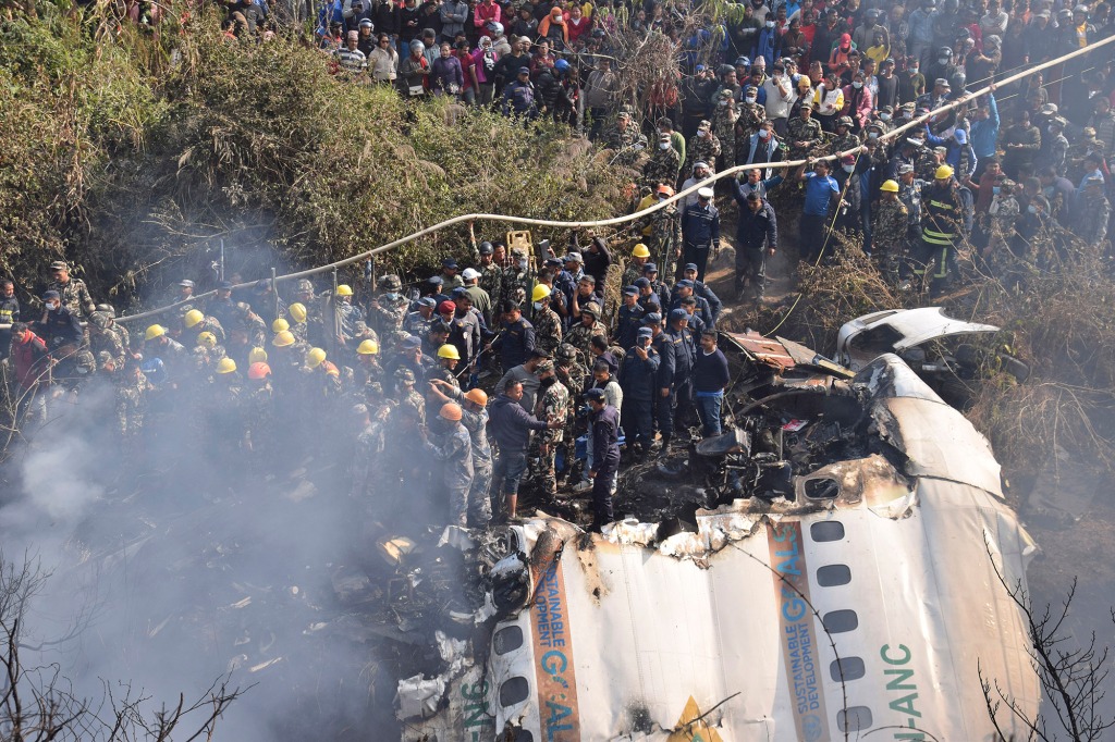 Nepalese rescue workers and civilians gather around the wreckage of a passenger plane.