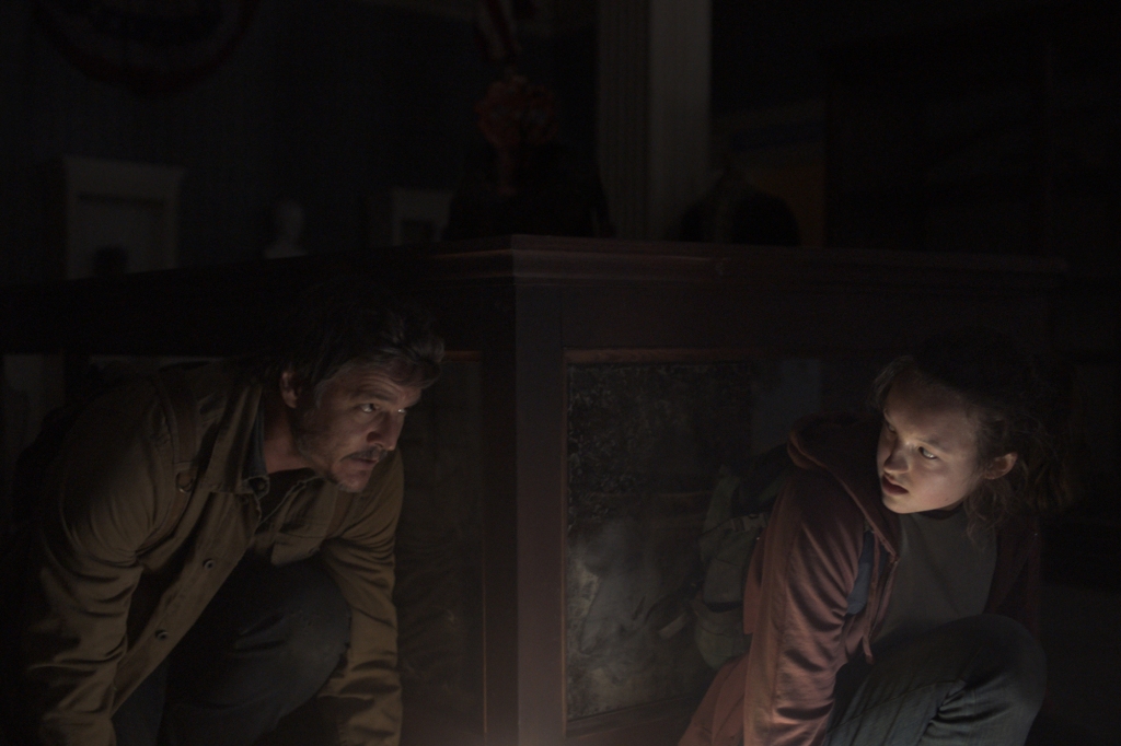 Pedro Pascal and Bella Ramsey in "The Last of Us" crouch in a dark room. 