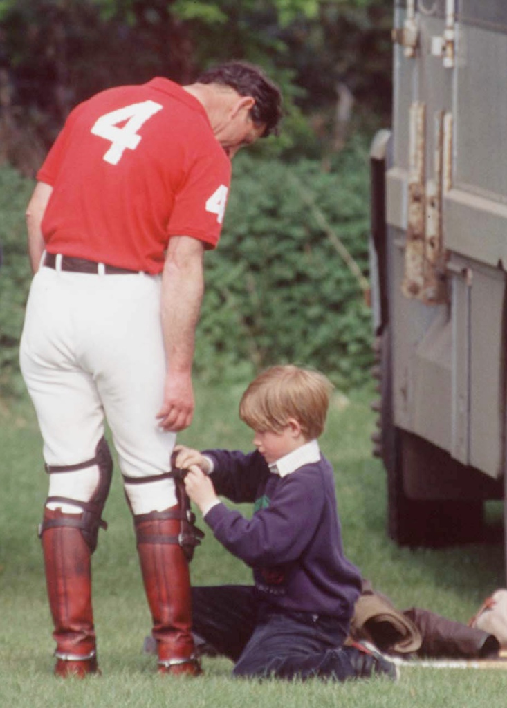 A young Prince Harry helps Prince Charles with his polo boots.