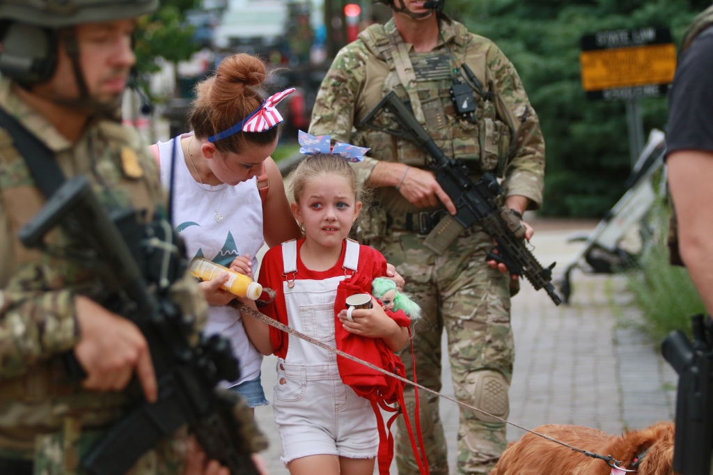 A young girl walking with her mother surrounded by soldiers with rifles