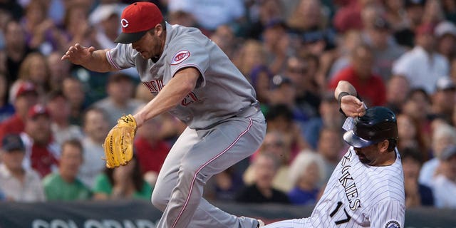 Scott Rolen #27 of the Cincinnati Reds leaps as Todd Helton #17 of the Colorado Rockies slides safely into third base in the sixth inning of a game at Coors Field on July 28, 2012 in Denver, Colorado. The Reds defeated the Rockies 9-7.