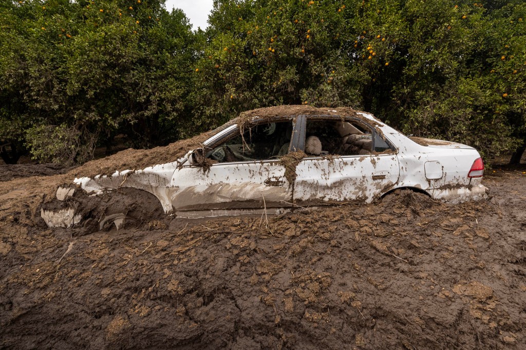 A car that was smashed by a landslide lies mud-bound on a closed road.