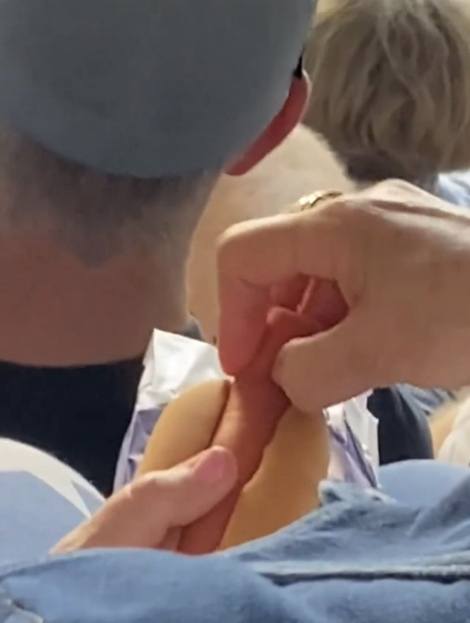 The tennis fan, instead of biting into the hot dog and bun, uses her hands and snaps off a tiny bite sized portion. 