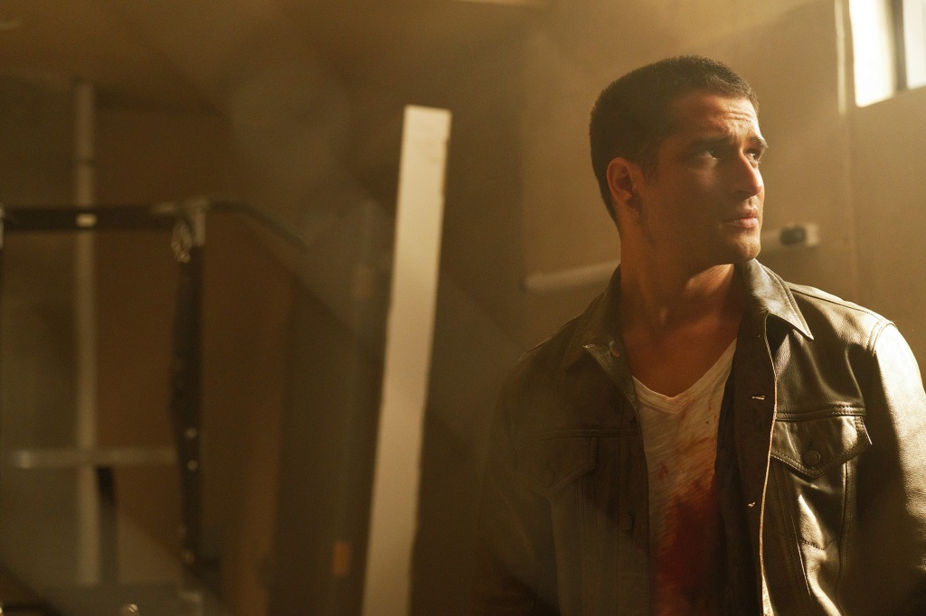 Tyler Posey as Scott McCall in "Teen Wolf: The Movie" looking serious wearing a leather jacket standing in a room. 