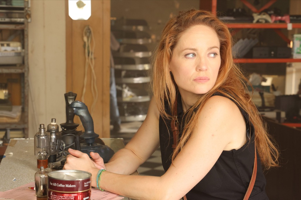 Erika Christensen as Det. Angie Polaski. She's sitting at a table and looking over her shoulder. There's a coffee can visible near her arm.