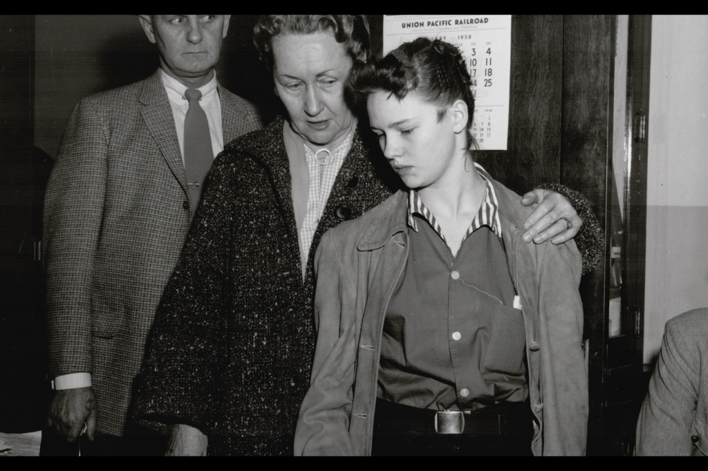 Photo of Fugate immediately after her arrest in 1958. She's wearing the coat of murder victim Clara Ward. An older woman has her arm around her shoulder as Caril looks down.