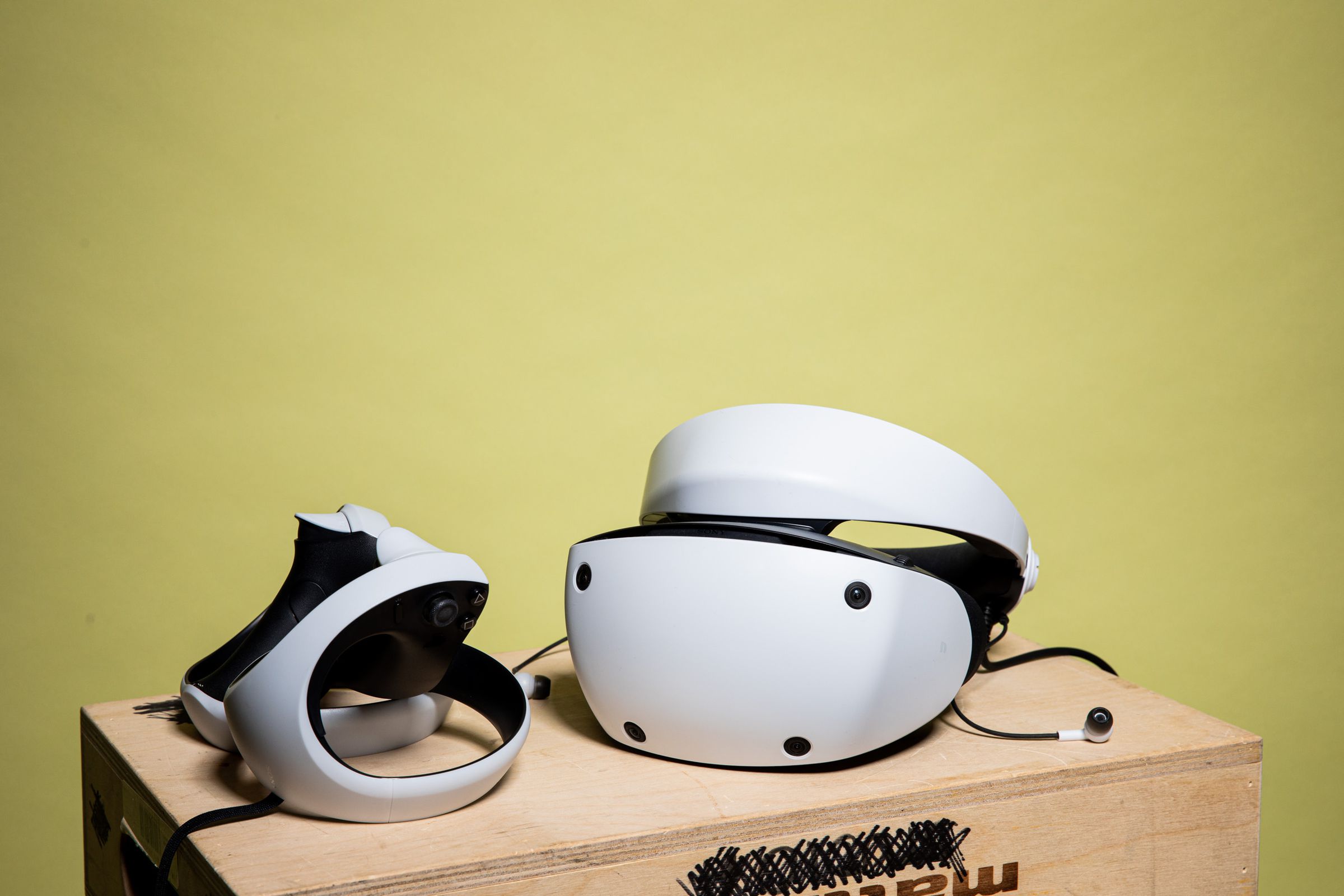 The headset and controllers sit on a wooden box, earbuds dangling out.