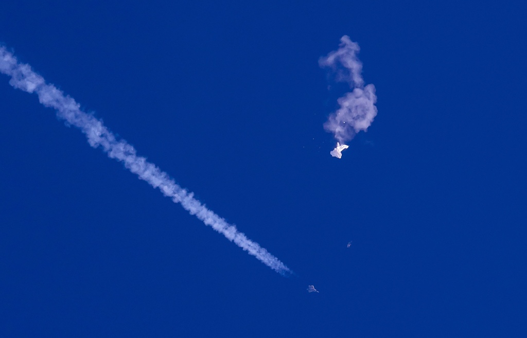 Remnants of the large balloon drift above the Atlantic Ocean, just off the coast of South Carolina, with a fighter jet and its contrail seen below it on Feb. 4.