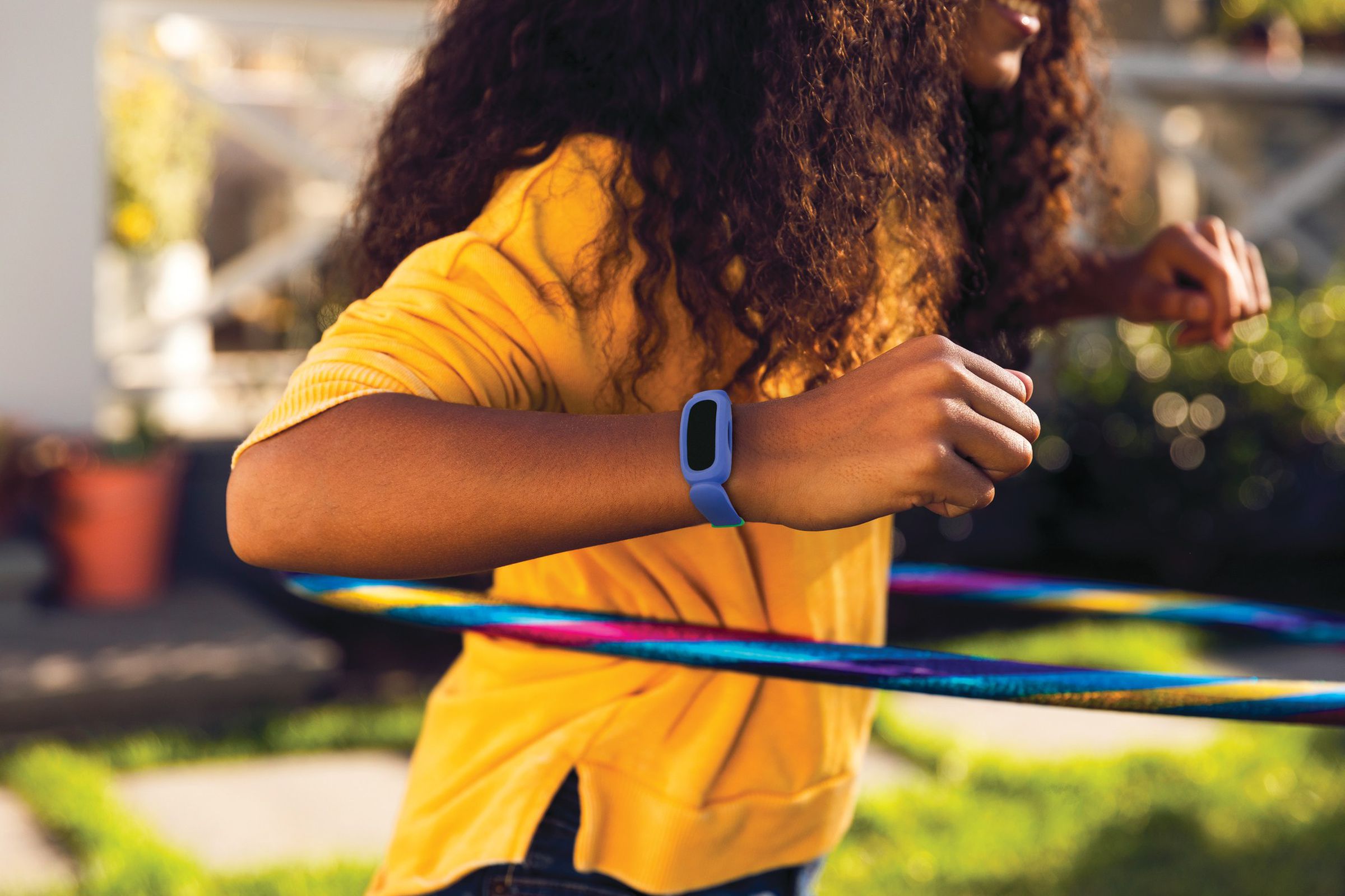 Photo of a child hula-hooping while wearing a blue Fitbit Ace on their right wrist. 