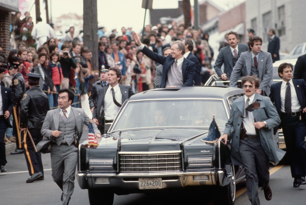 President Jimmy Carter stands through the sunroof of his limousine as Secret Service agents run alongside him in New Jersey on Oct. 25, 1979.