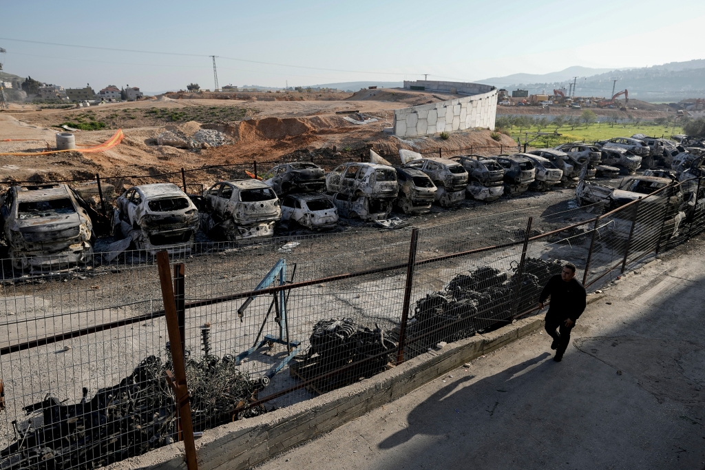 A Palestinian man walks past burned cars in the town of Hawara, near the West Bank city of Nablus, Monday, Feb. 27, 2023. 