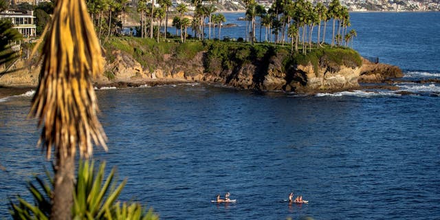 Paddle boarders take a scenic sunset cruise amidst warm weather in Crescent Bay Beach in Laguna Beach, California.