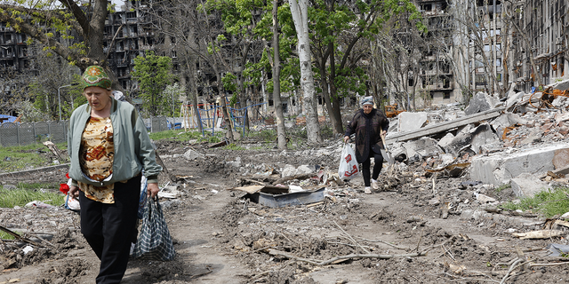 Women walk past a destroyed apartment building in Mariupol, in territory under the government of the Donetsk People's Republic, on May 2, 2022.