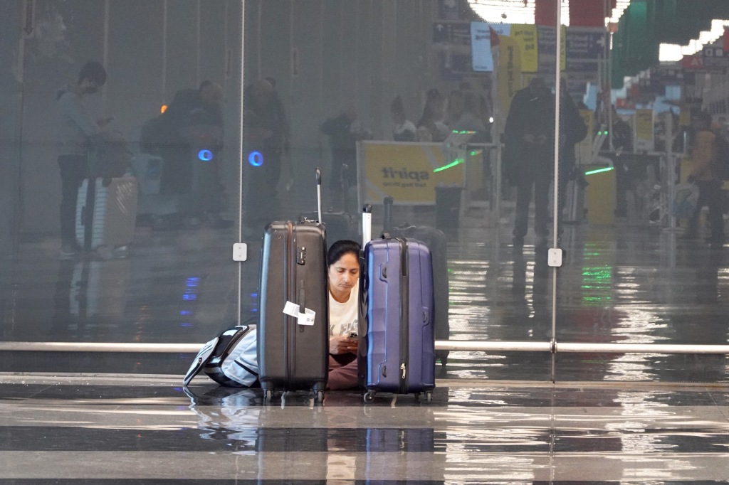 A picture of a woman sitting on the floor at an airport.