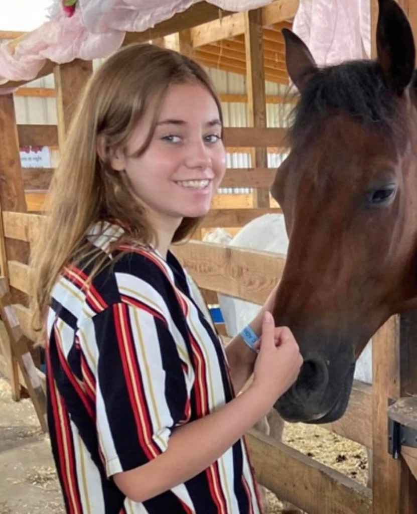 Adriana Kuch, a young teen, poses while petting a horse in a barn.