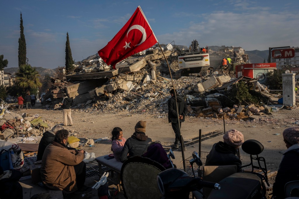 A family sits near a collapsed building as they wait for bodies of their relatives to be recovered.