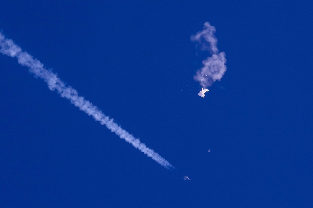 In this photo provided by Chad Fish, the remnants of a large balloon drift above the Atlantic Ocean, just off the coast of South Carolina, with a fighter jet and its contrail seen below it, Feb. 4, 2023.