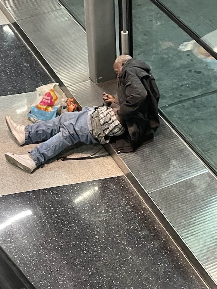 A pciture of a homeless man on the floor at an airport.