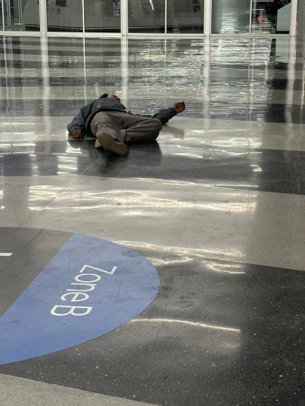 A homeless man on the floor at an airport.