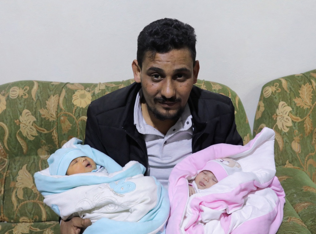 Khalil Al-Sawadi, holding his niece and adopted daughter Afraa in a pink blanket. In his other arm, wrapped in a blue blanket, his own newborn, Ataa, who was born three days after the quake.